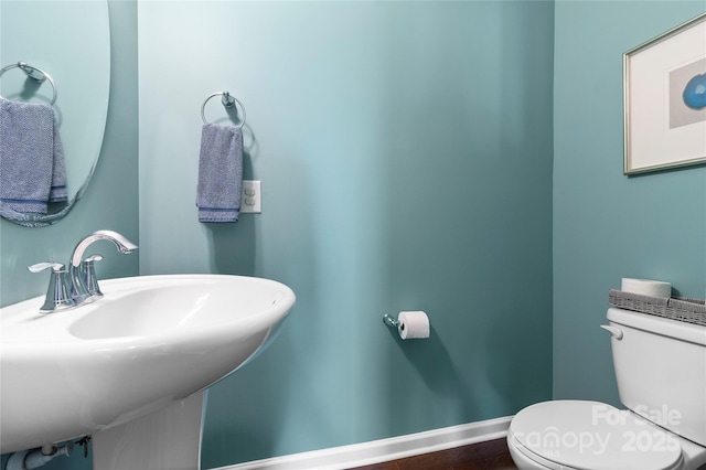 half bathroom featuring baseboards, a sink, and toilet