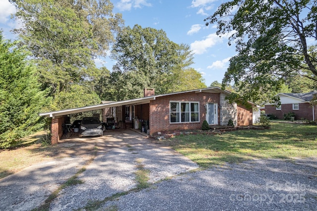 ranch-style house featuring a chimney, driveway, an attached carport, a front yard, and brick siding