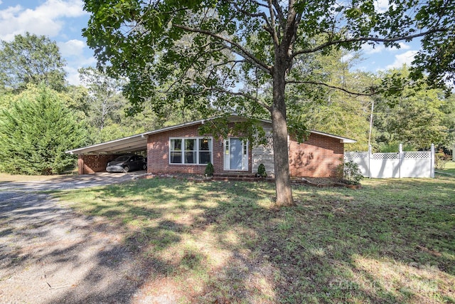 view of front facade with an attached carport, fence, brick siding, gravel driveway, and a front yard