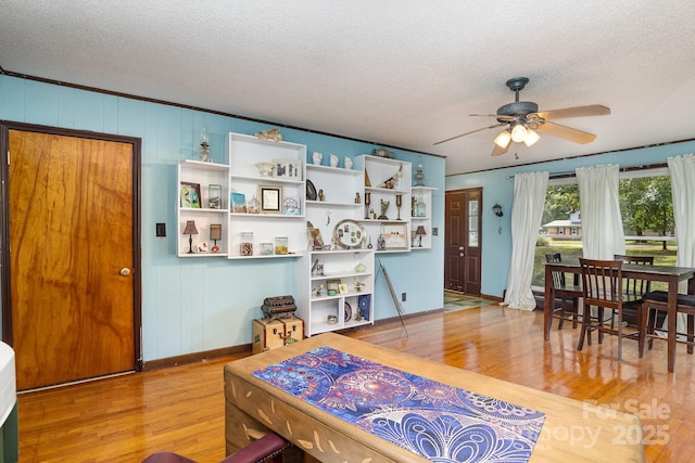 living area with baseboards, a ceiling fan, wood finished floors, and a textured ceiling