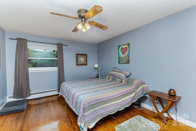 bedroom featuring a baseboard heating unit, wood finished floors, baseboards, and ceiling fan