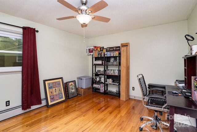 office space with light wood finished floors, a ceiling fan, and a baseboard radiator
