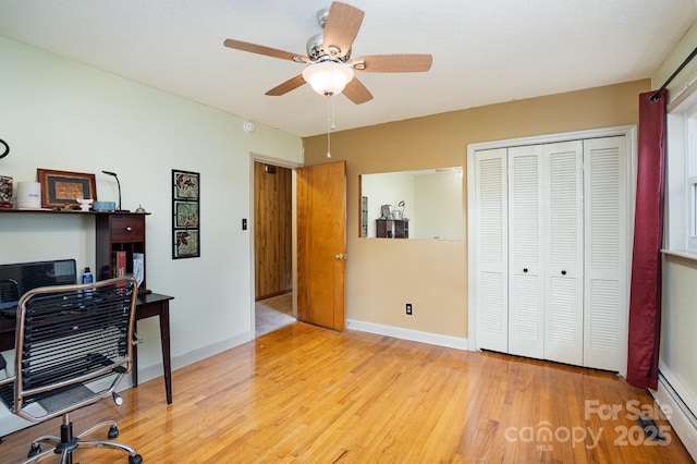 home office with a baseboard heating unit, wood finished floors, a ceiling fan, and baseboards
