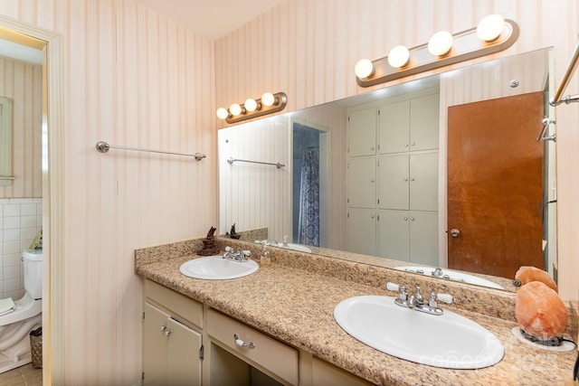 full bath featuring wallpapered walls, double vanity, toilet, and a sink