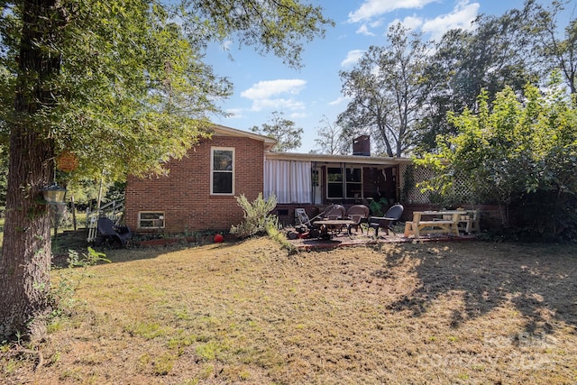 back of house featuring a chimney, brick siding, a yard, and a patio