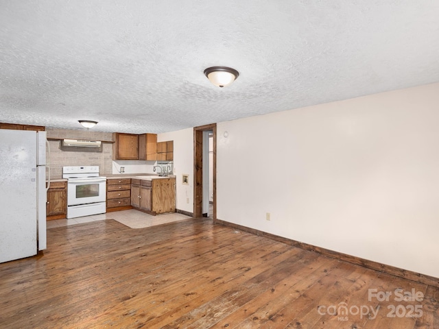 kitchen featuring brown cabinetry, a sink, baseboards, ventilation hood, and white appliances