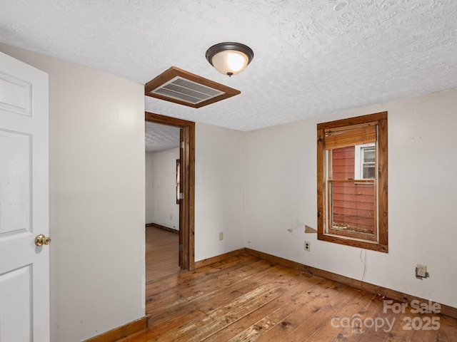 unfurnished room featuring a textured ceiling, visible vents, baseboards, and hardwood / wood-style floors