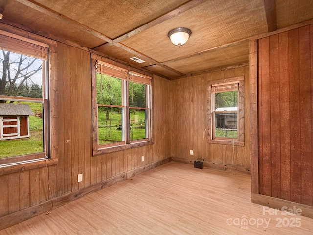 unfurnished room with wooden walls, a wealth of natural light, wood finished floors, and visible vents