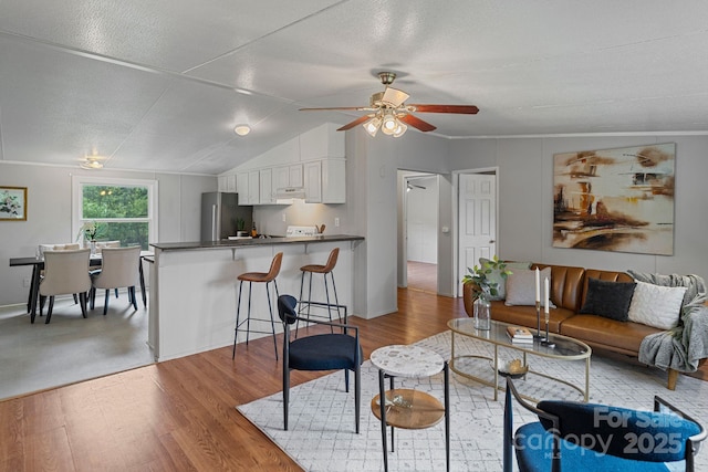 living area featuring light wood finished floors, ceiling fan, and vaulted ceiling