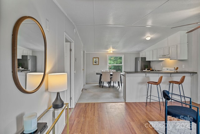 kitchen featuring dark countertops, white cabinets, freestanding refrigerator, and lofted ceiling