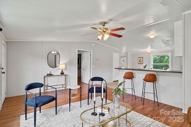 interior space with lofted ceiling, baseboards, a textured ceiling, a ceiling fan, and light wood-style flooring