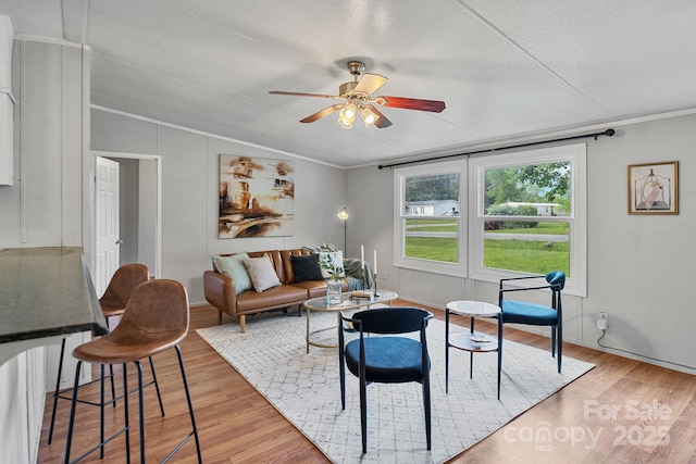 living room featuring a ceiling fan, a textured ceiling, crown molding, light wood finished floors, and lofted ceiling