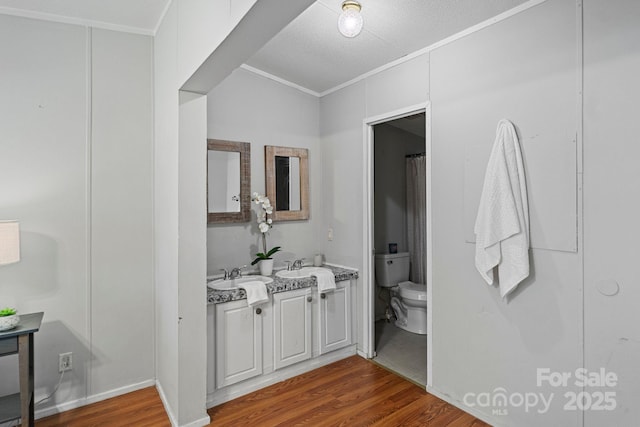 full bath featuring double vanity, wood finished floors, a sink, toilet, and ornamental molding