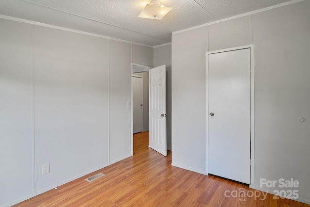 unfurnished bedroom with visible vents, ornamental molding, a decorative wall, and light wood-type flooring