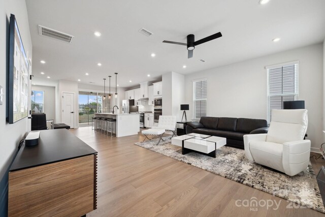 living area with light wood finished floors, a ceiling fan, visible vents, and recessed lighting