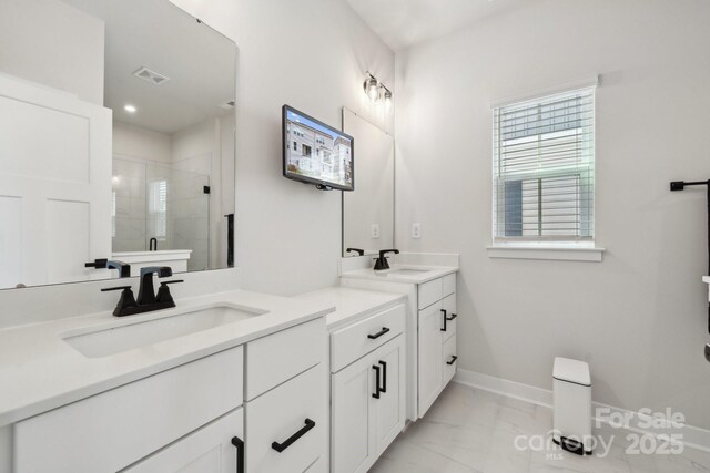 full bath with a sink, a stall shower, marble finish floor, two vanities, and baseboards