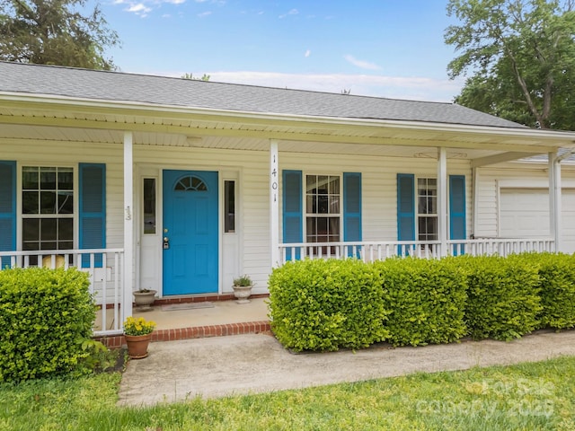 view of exterior entry with a porch, a shingled roof, and an attached garage