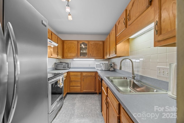 kitchen with brown cabinets, a sink, appliances with stainless steel finishes, light countertops, and under cabinet range hood