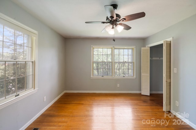 unfurnished bedroom with baseboards, a closet, wood finished floors, and multiple windows