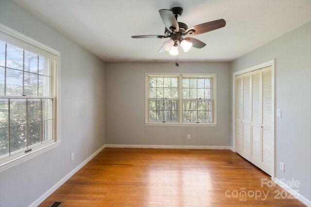 unfurnished bedroom featuring light wood-type flooring, baseboards, a closet, and multiple windows