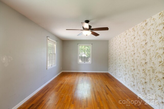 empty room featuring baseboards, ceiling fan, wallpapered walls, and wood finished floors