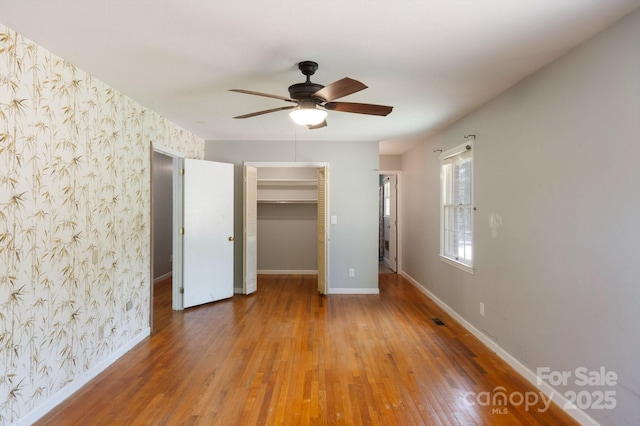 unfurnished bedroom featuring baseboards, wallpapered walls, wood finished floors, and a spacious closet