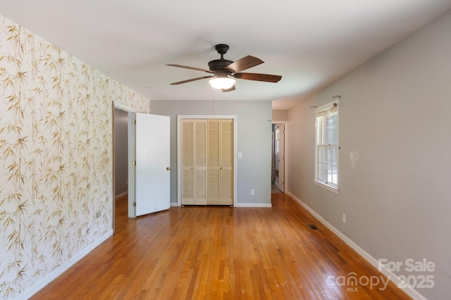 unfurnished bedroom featuring baseboards, wallpapered walls, wood finished floors, and a closet