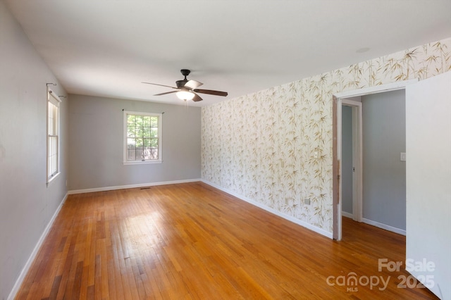 spare room featuring baseboards, wallpapered walls, a ceiling fan, and light wood-type flooring