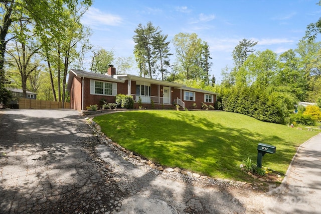 single story home featuring fence, aphalt driveway, brick siding, a porch, and a chimney