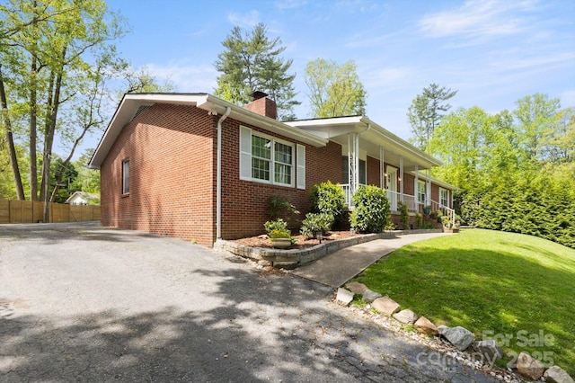 view of side of property featuring fence, a chimney, brick siding, a porch, and a yard