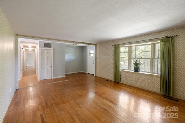 empty room with baseboards, wood-type flooring, wallpapered walls, and visible vents