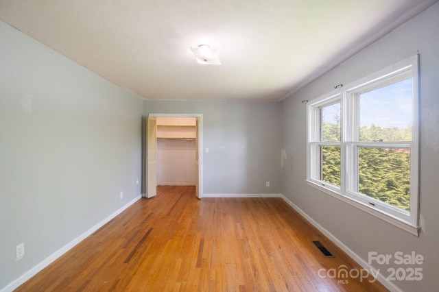 unfurnished bedroom featuring light wood-type flooring, baseboards, visible vents, and a spacious closet