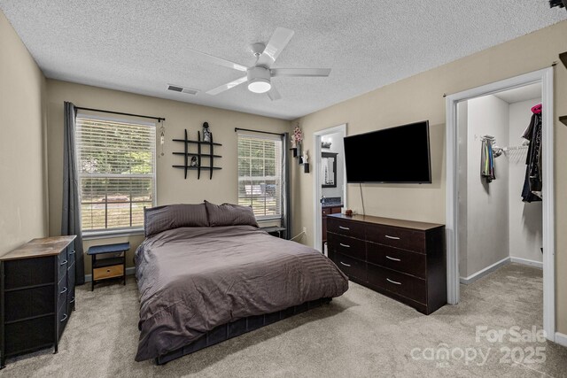 bedroom with a walk in closet, a textured ceiling, visible vents, light colored carpet, and a closet