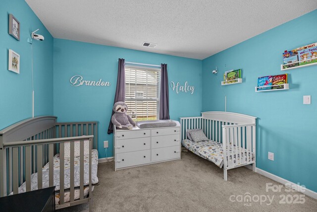 bedroom with a nursery area, baseboards, carpet, and a textured ceiling
