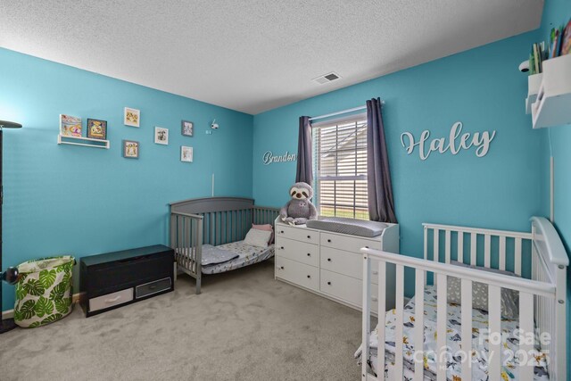 bedroom with visible vents, carpet flooring, a textured ceiling, and a crib
