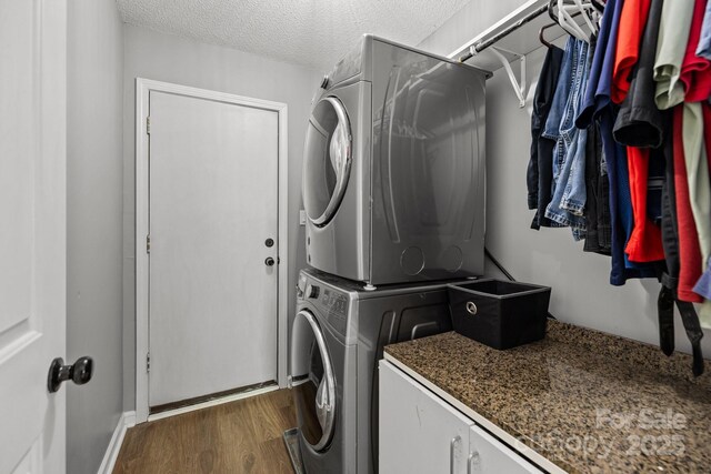 laundry area featuring laundry area, a textured ceiling, stacked washer / dryer, dark wood finished floors, and baseboards