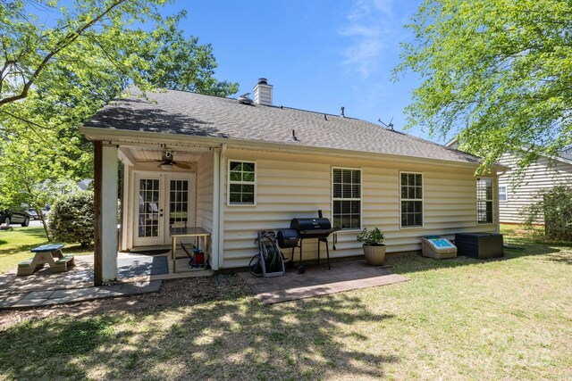 rear view of property featuring ceiling fan, a chimney, a yard, a patio, and a shingled roof