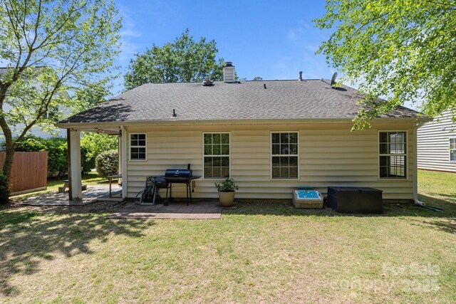 rear view of property with fence, roof with shingles, a chimney, a patio area, and a lawn