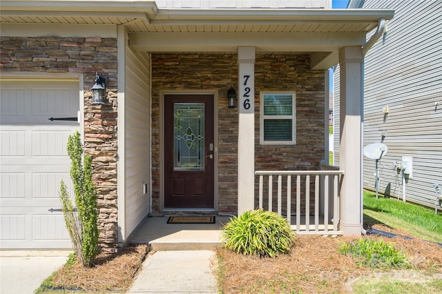 doorway to property with covered porch, an attached garage, and stone siding