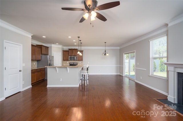 kitchen featuring a kitchen bar, brown cabinets, a ceiling fan, appliances with stainless steel finishes, and backsplash