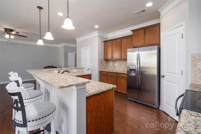 kitchen with visible vents, brown cabinetry, a breakfast bar, and stainless steel fridge with ice dispenser