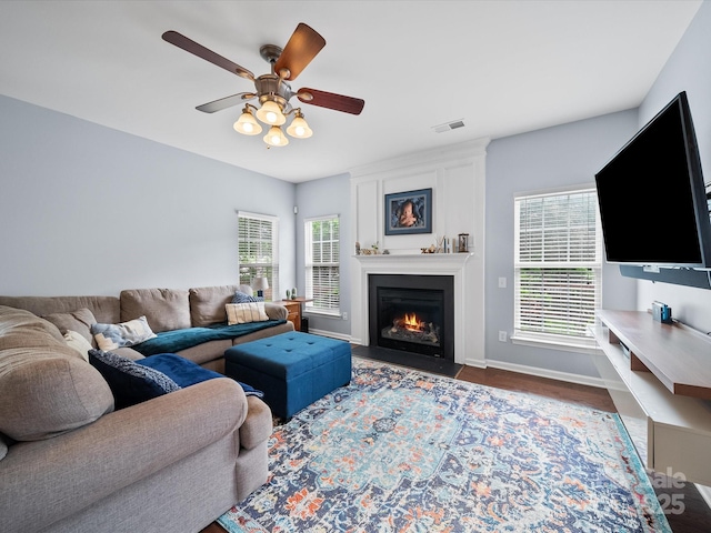 living area with a fireplace, ceiling fan, visible vents, baseboards, and wood finished floors