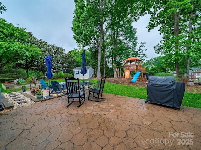 view of patio / terrace featuring a playground, an outbuilding, outdoor dining area, a storage shed, and fence