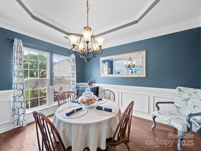 dining room featuring a notable chandelier, a raised ceiling, crown molding, wainscoting, and wood finished floors