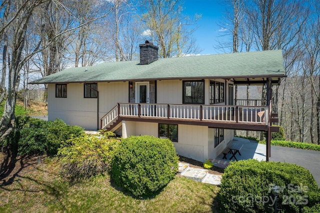 rear view of property with stairway, roof with shingles, a chimney, and a deck
