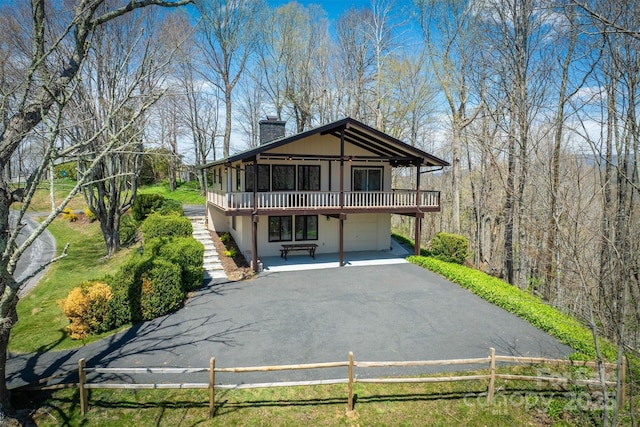 exterior space featuring aphalt driveway, fence, a deck, a chimney, and an attached garage