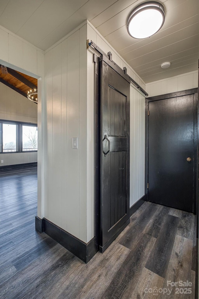 hallway featuring wooden walls, baseboards, dark wood-style floors, and a barn door