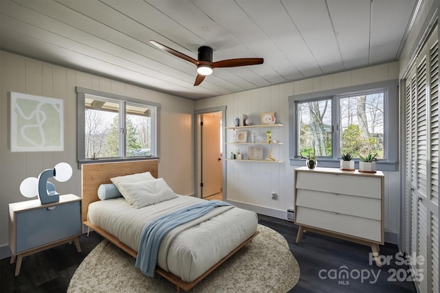 bedroom with wooden walls, a ceiling fan, and dark wood finished floors