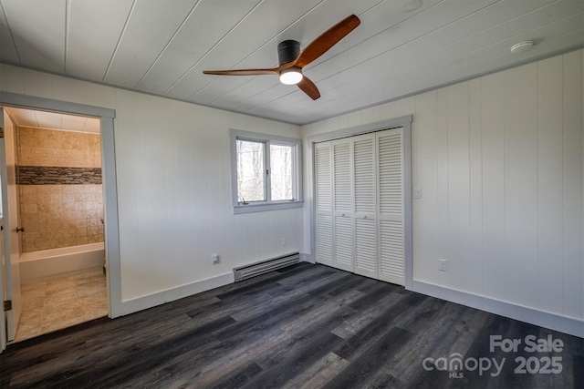 unfurnished bedroom with a closet, baseboards, a baseboard heating unit, and dark wood-style flooring