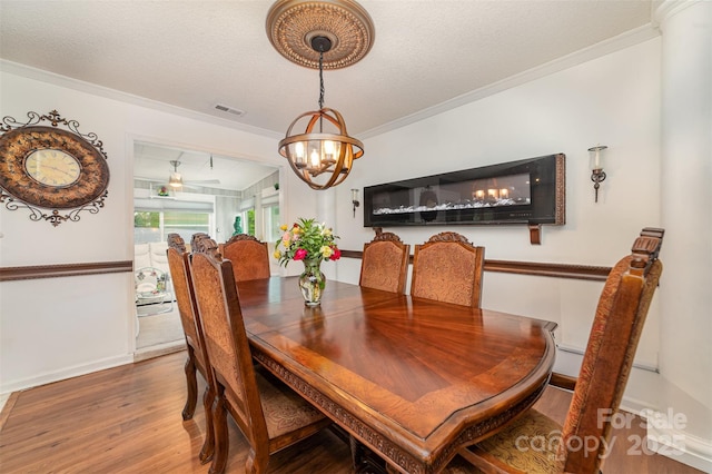 dining space featuring a chandelier, baseboards, wood finished floors, visible vents, and ornamental molding